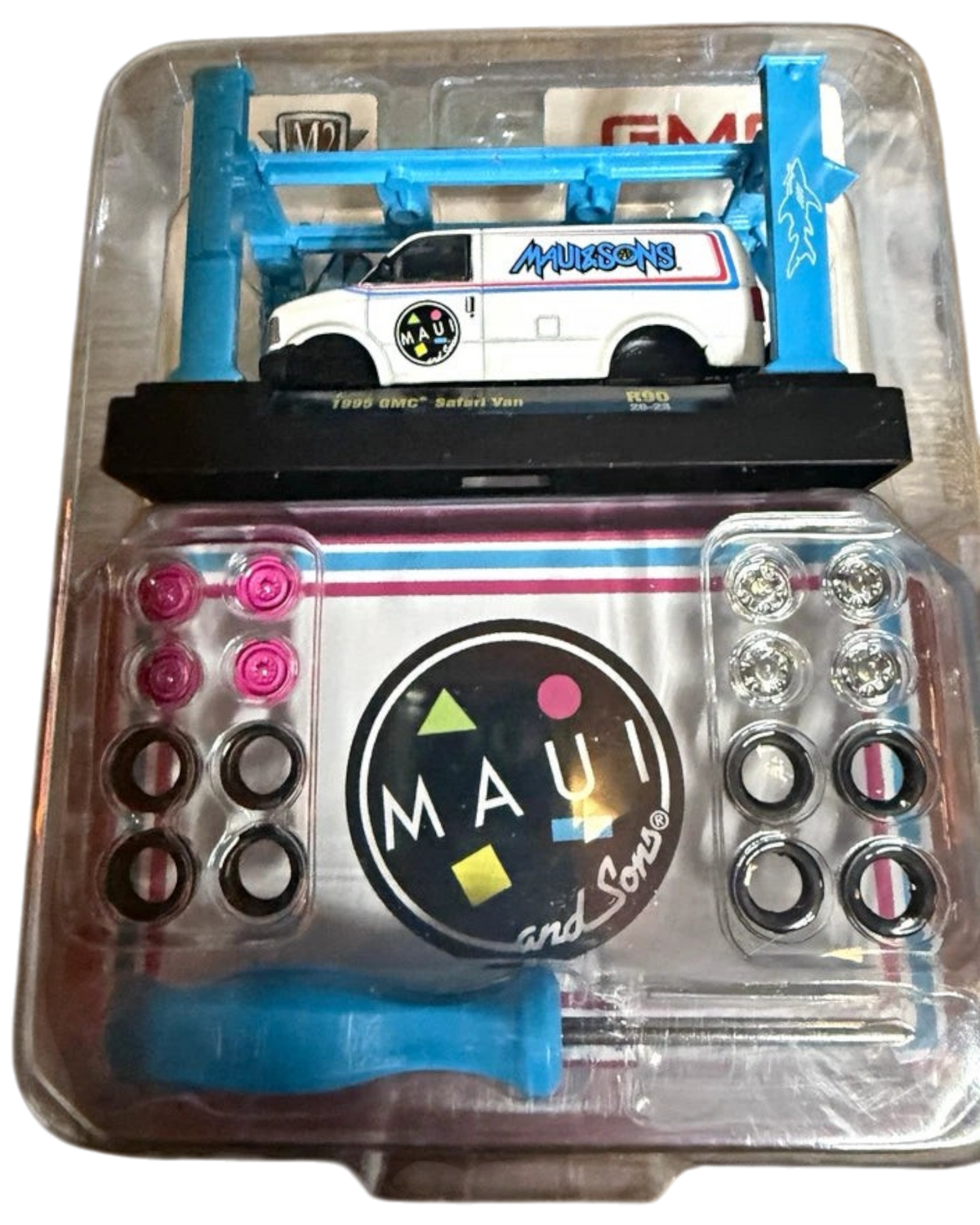 More Than Diecast 1:64 scale 1995 GMC Safari Van model kit in white with Maui and Sons graphics on a blue display lift