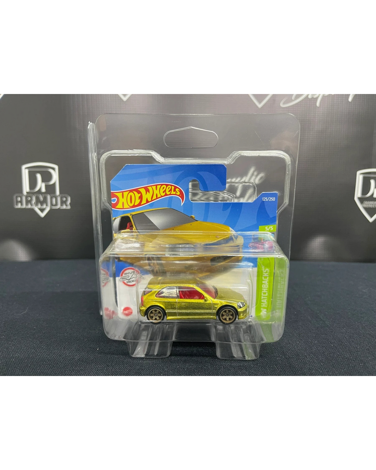 More Than Diecast Diamond Short Card Protector holding a gold Hot Wheels hatchback toy car in clear PVC packaging